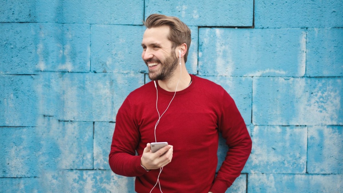 Ein Mann steht vor einer blauen Wand mit seinem Smartphone in der Hand.