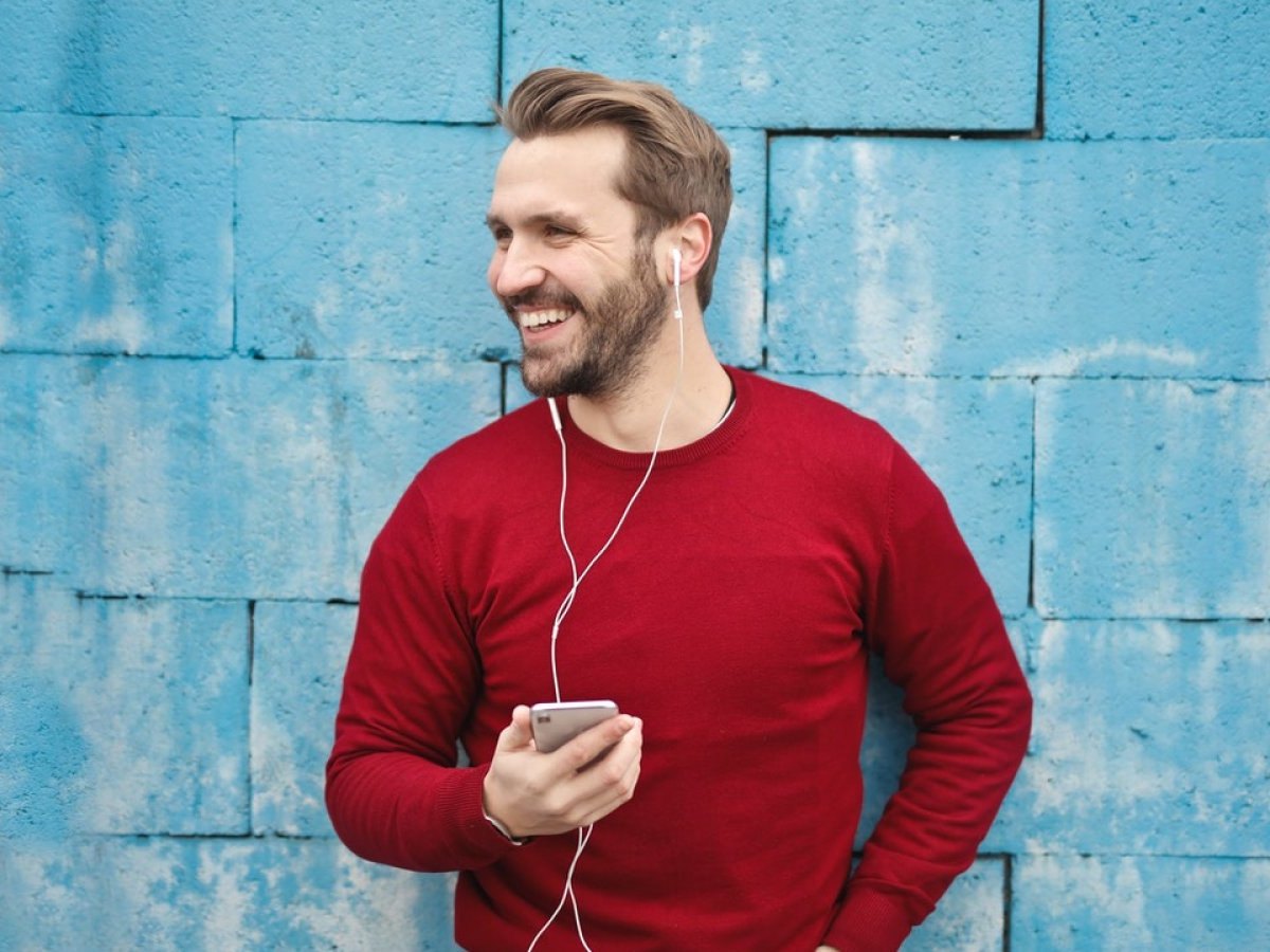 Ein Mann steht vor einer blauen Wand mit seinem Smartphone in der Hand.