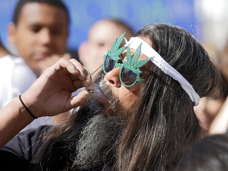 Mann mit Brille in Form von Haschisch-Blättern raucht einen Joint.
