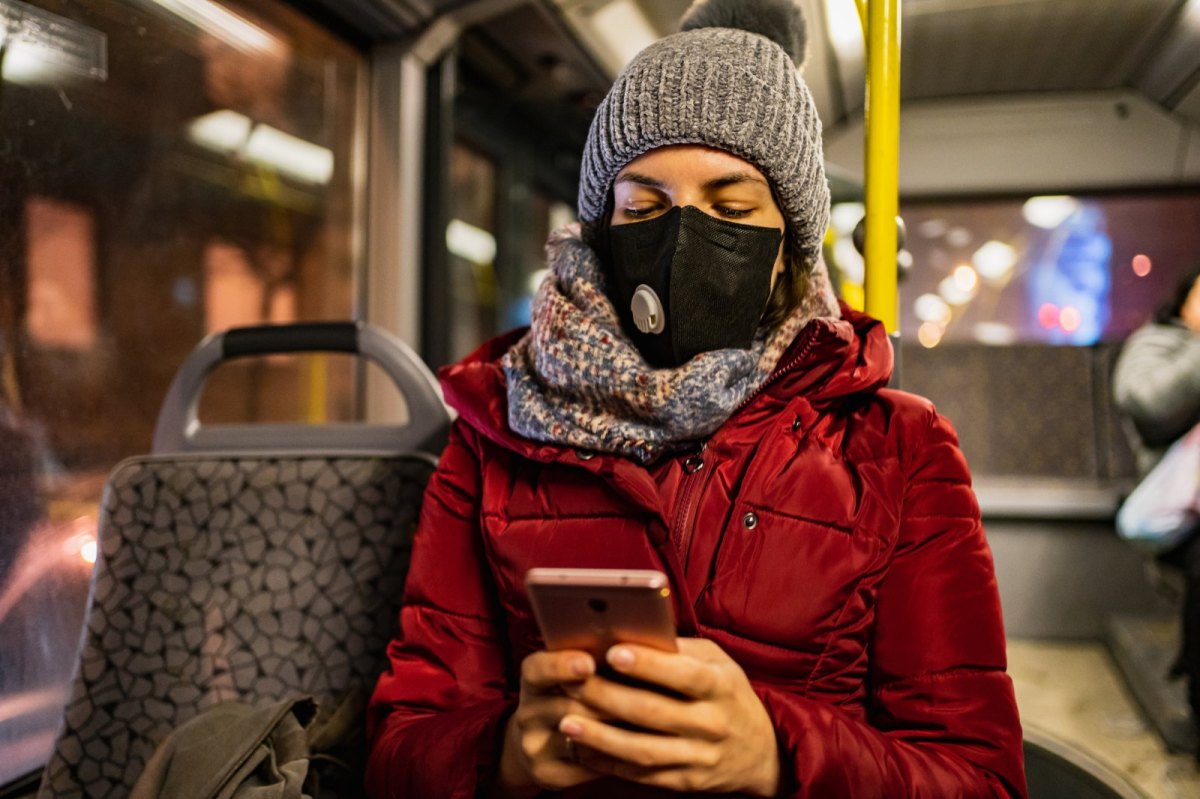 Frau mit Winterbekleidung und Maske im Bus.