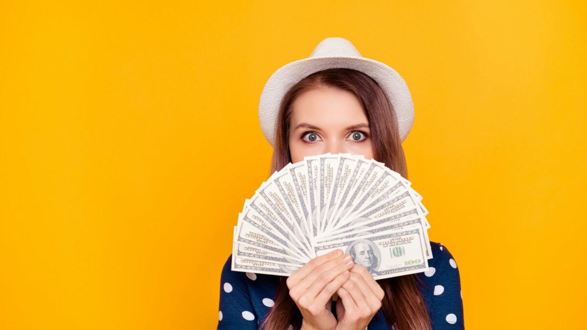Frau hält einen Fächer aus Dollar-Noten vor ihr Gesicht