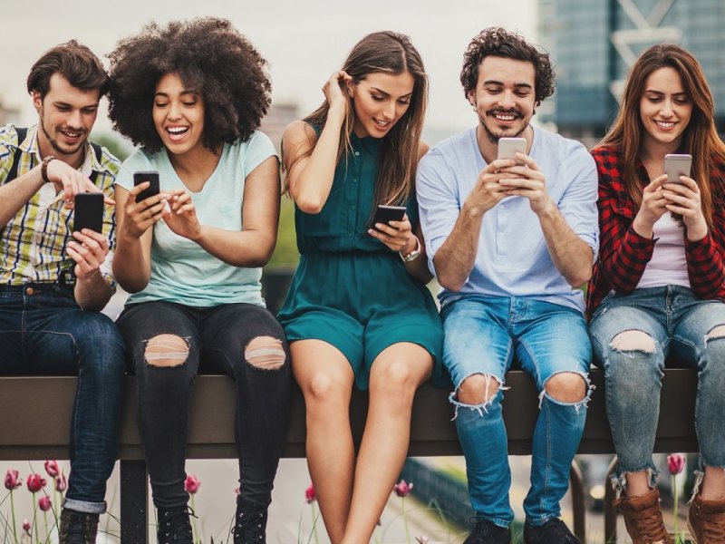 Fünf Freunde blicken alle auf ihr eigenes Handy und lächeln.