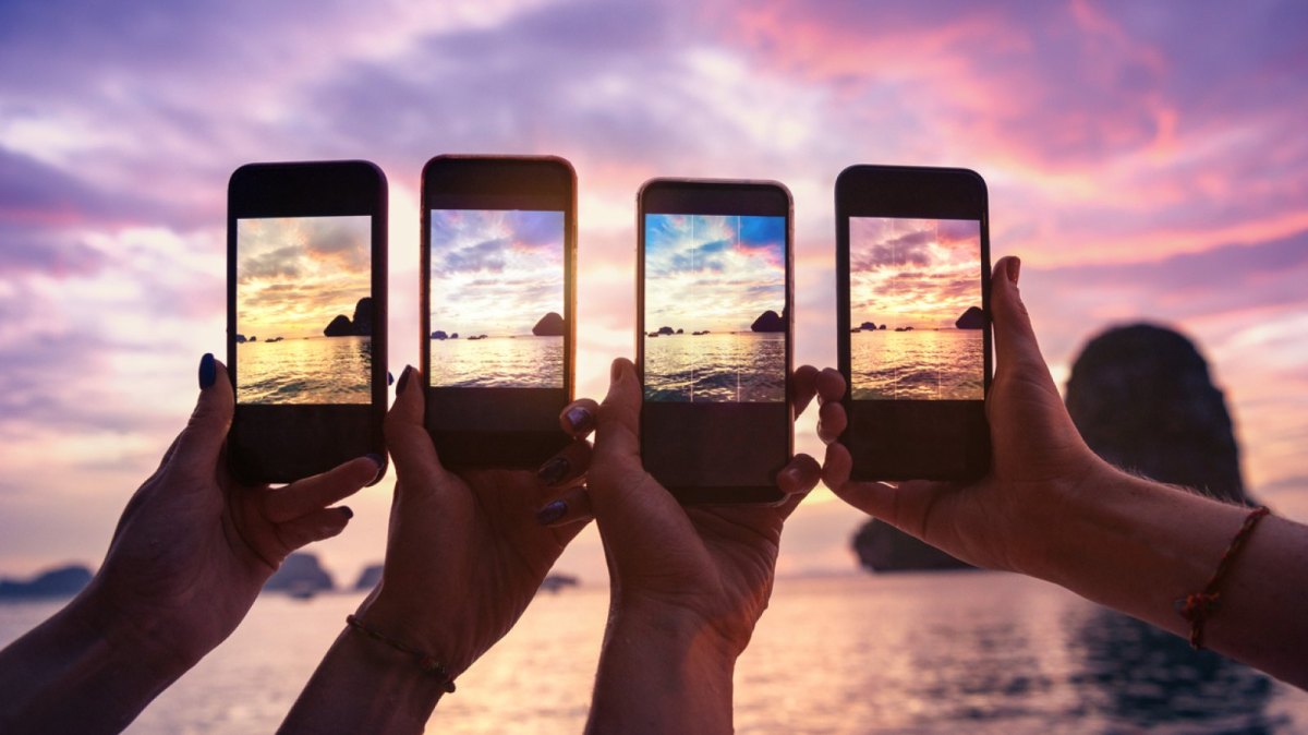 Vier Handys machen ein Bild eines Sonnenuntergangs.