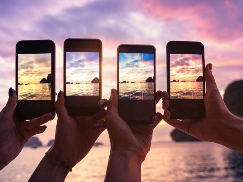 Vier Handys machen ein Bild eines Sonnenuntergangs.