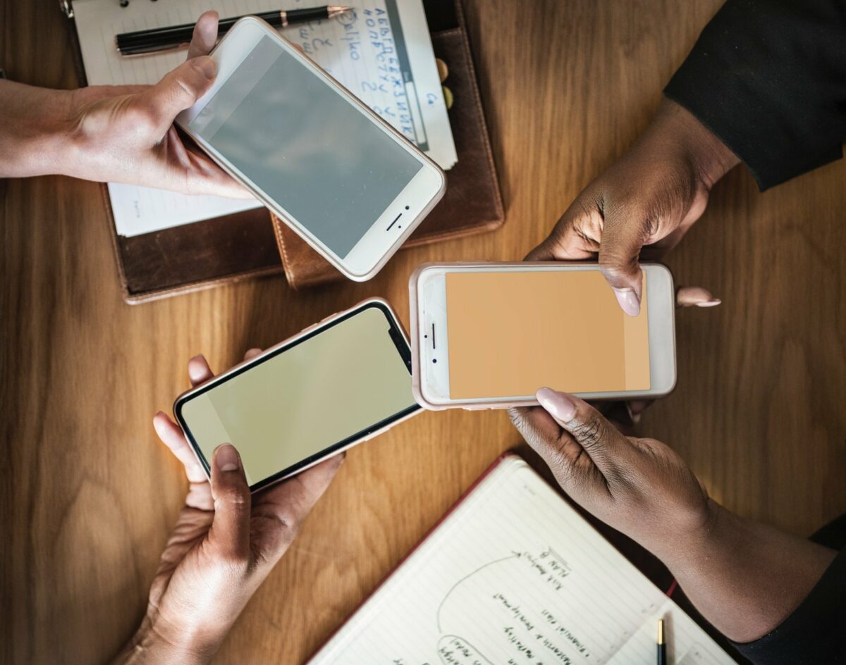 Drei Smartphones werden über einem Tisch mit Dokumenten drauf in den Händen gehalten.