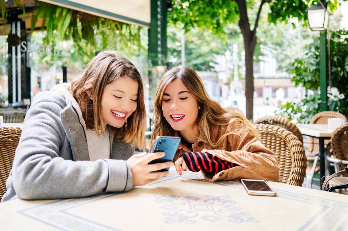 Zwei Freundinnen schauen fröhlich auf ein Handy.