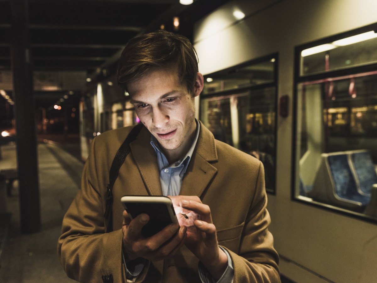 Mann schaut neben einer Straßenbahn auf sein Smartphone