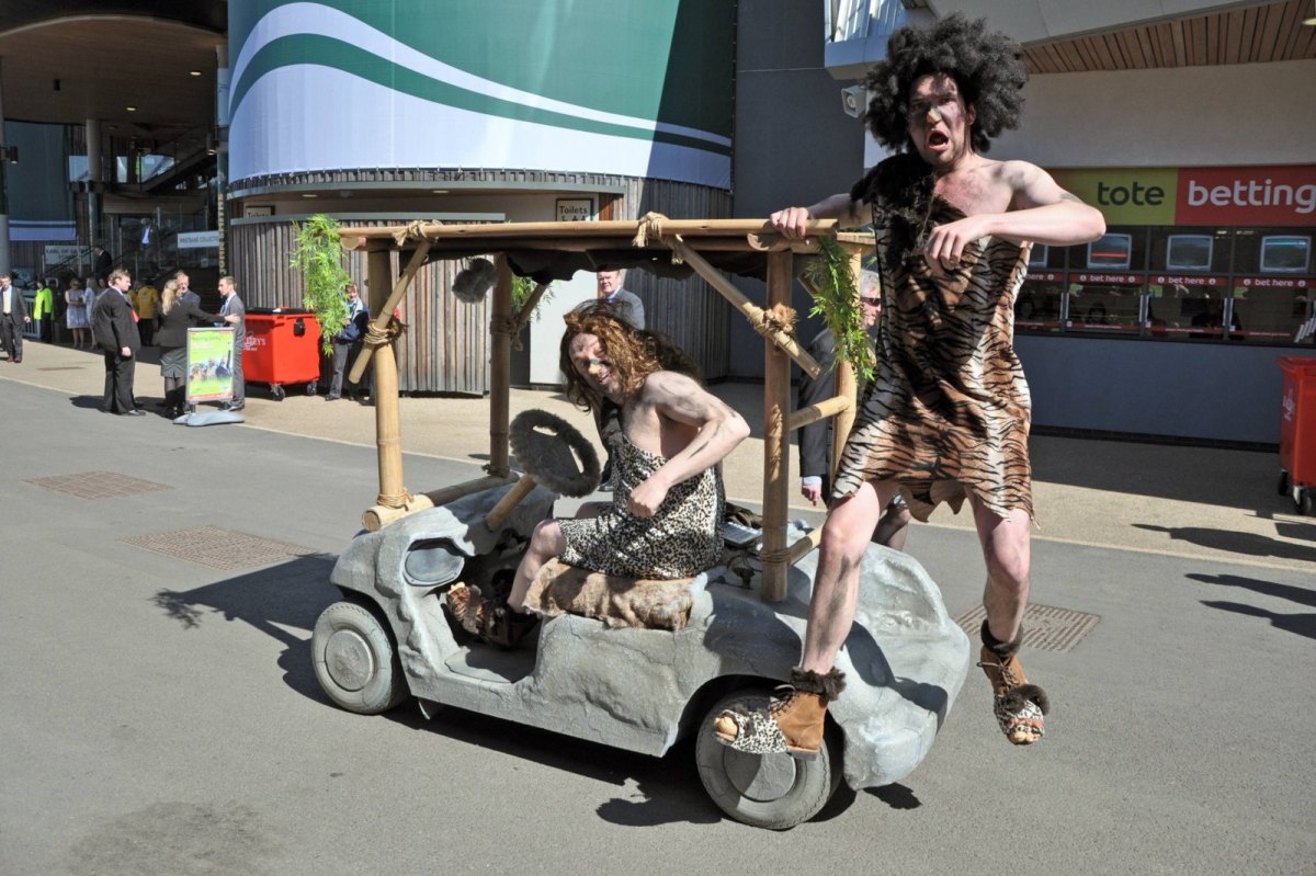 Männer als Neandertaler verkleidet fahren auf Steinzeit-Mobil.