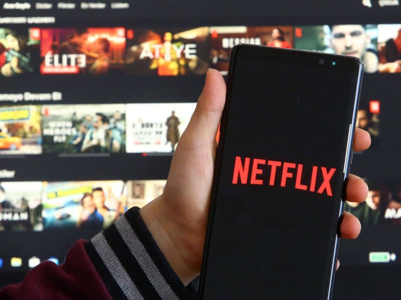 Ein Handy mit dem Netflix-Logo vor einem Fernseher mit Netflix-Oberfläche.