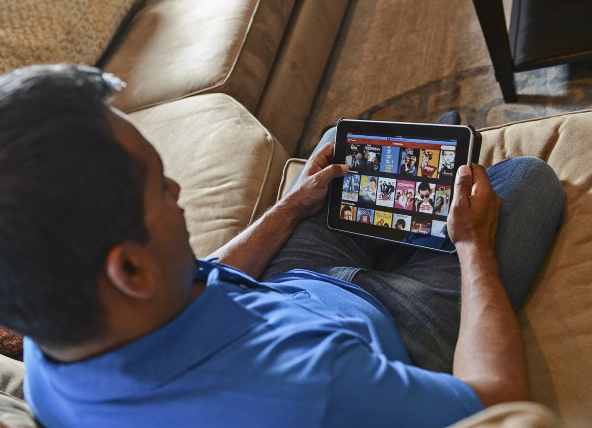 Mann sitzt auf Couch und schaut auf sein Tablet mit Netflix-Angeboten