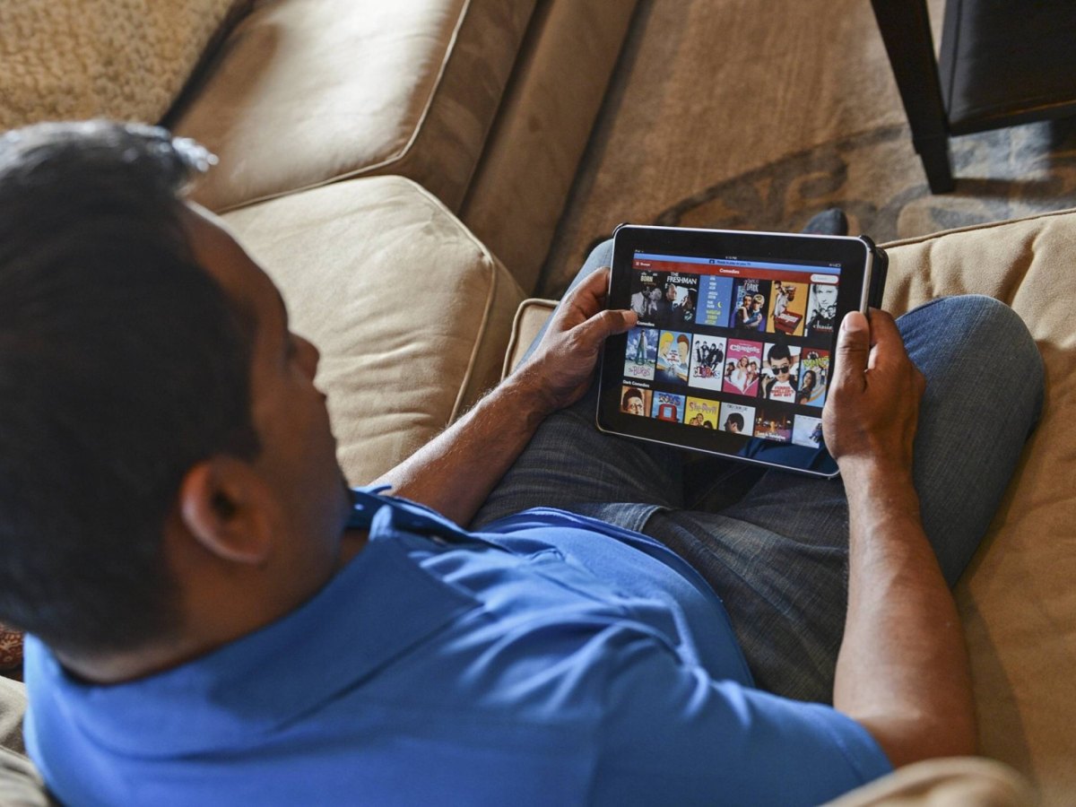 Mann sitzt auf Couch und schaut auf sein Tablet mit Netflix-Angeboten