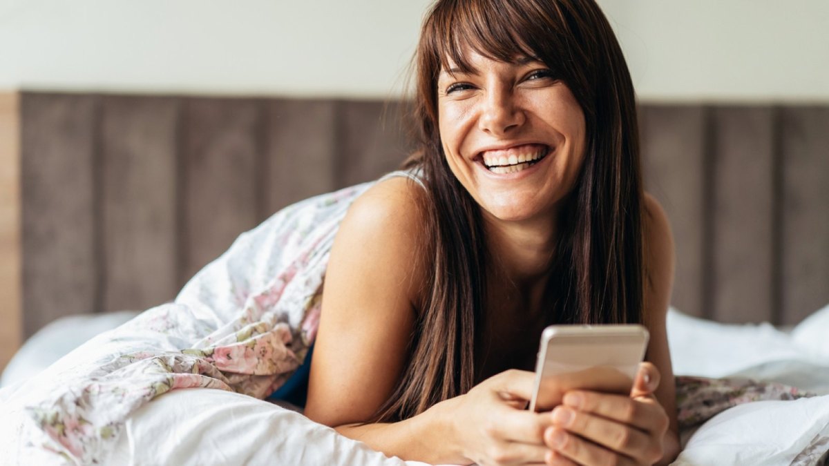 Frau mit Handy in der Hand im Bett.