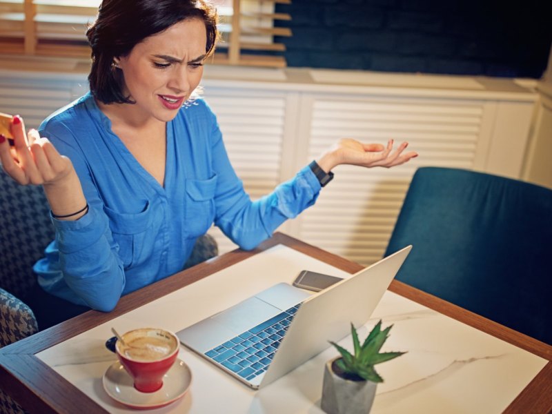 Frau mit Kreditkarte wütend am Laptop.