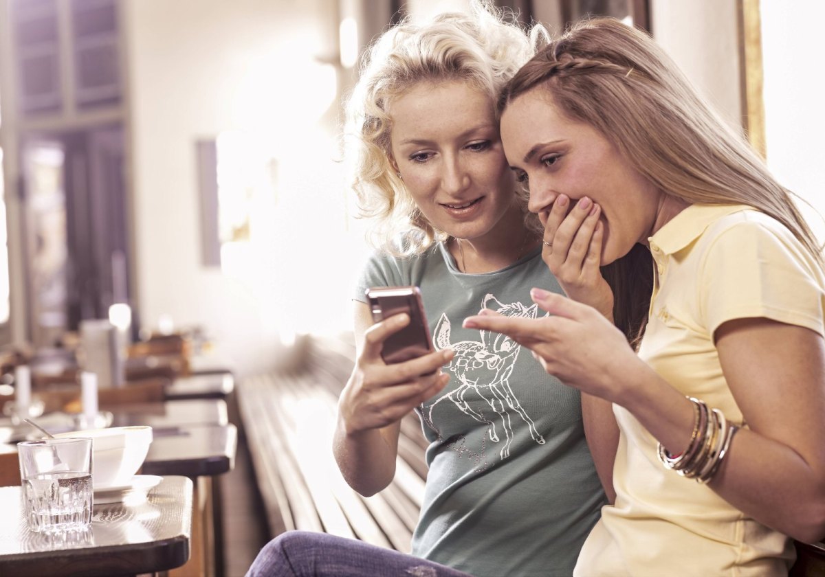 Frauen sehen peinlich berührt auf ein Smartphone