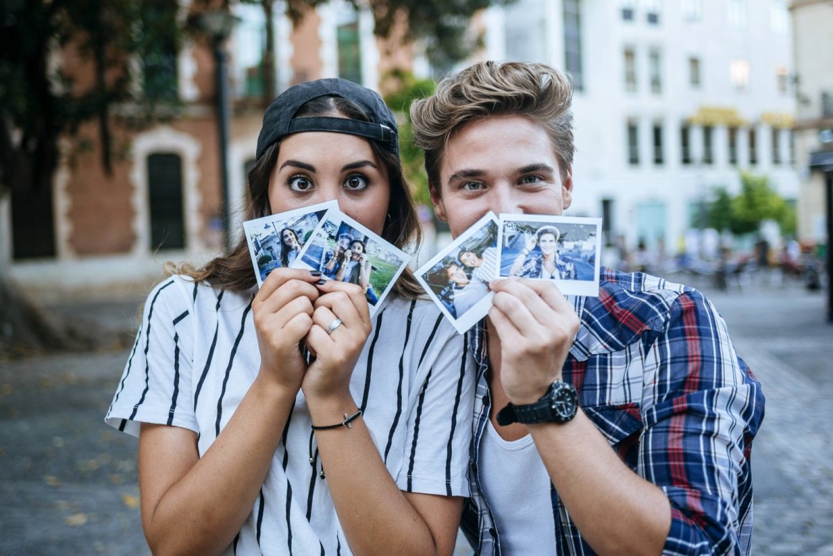 Zwei Freunde halten sich Polaroid-Kamera Fotos vor das Gesicht.