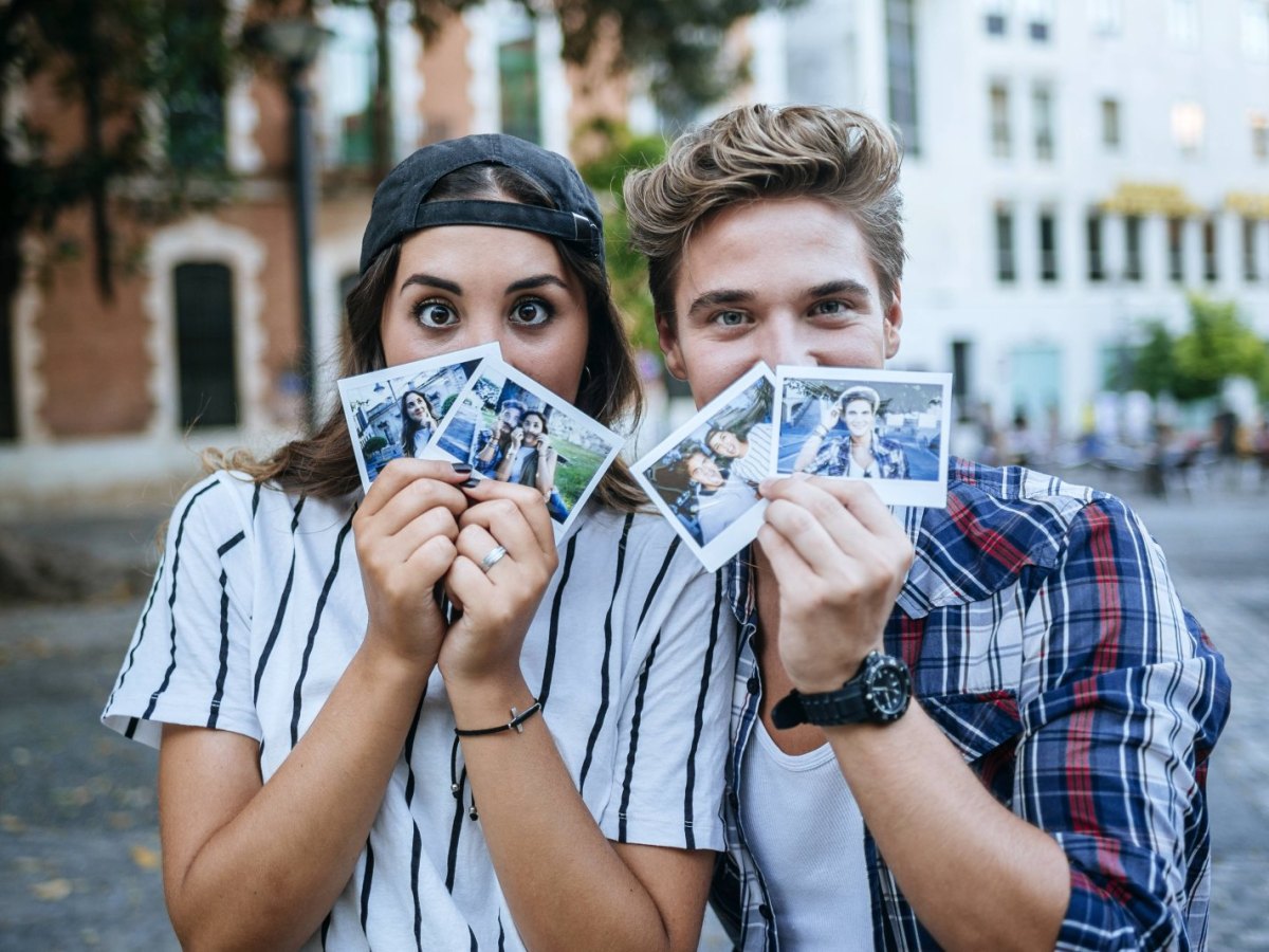 Zwei Freunde halten sich Polaroid-Kamera Fotos vor das Gesicht.