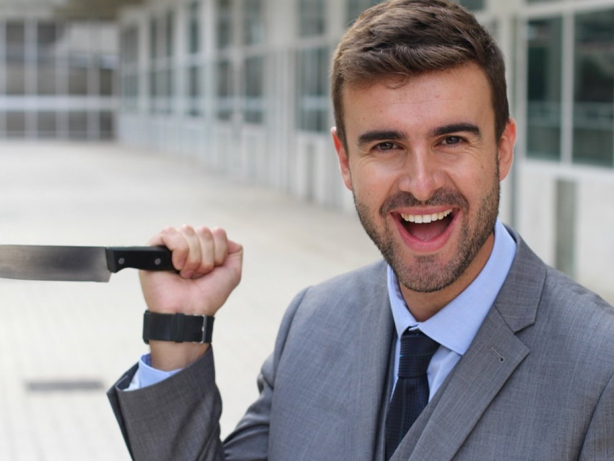 Lächelnder Geschäftsmann mit einem Messer in der Hand.