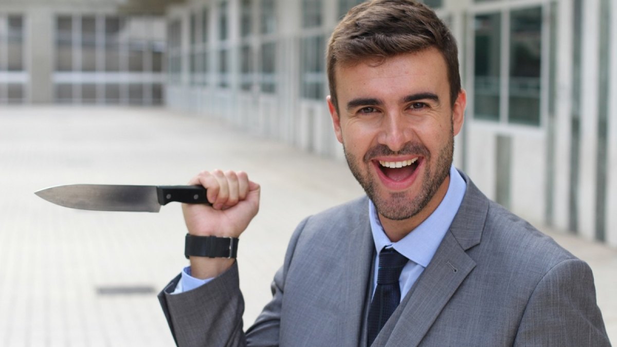 Lächelnder Geschäftsmann mit einem Messer in der Hand.