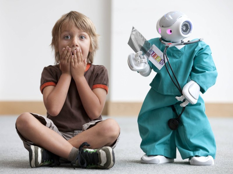 Kind sitzt neben Roboter im Arztkittel und hält sich den Mund zu