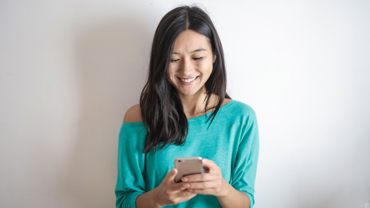 Eine Frau schaut auf ihr Smartphone und lächelt.