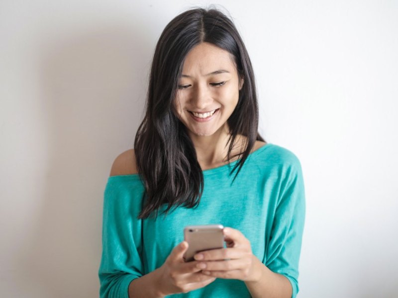 Eine Frau schaut auf ihr Smartphone und lächelt.