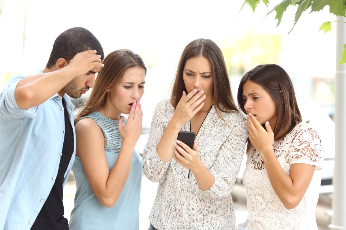 Vier Personen blicken schockiert auf ein Smartphone