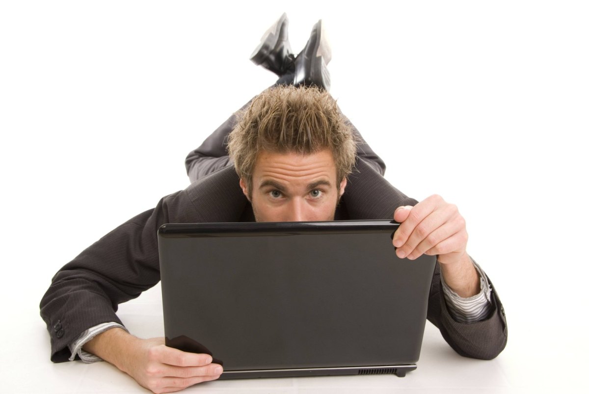 Mann im Anzug auf dem Bauch liegend versteckt sein halbes Gesicht hinter einem Laptop
