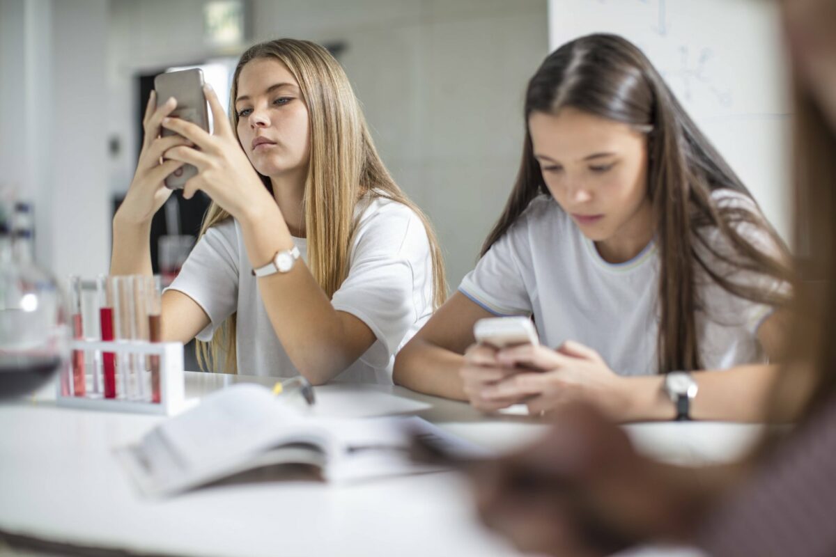 Zwei Schülerinnen schauen im Unterricht genervt auf ihre Handys.