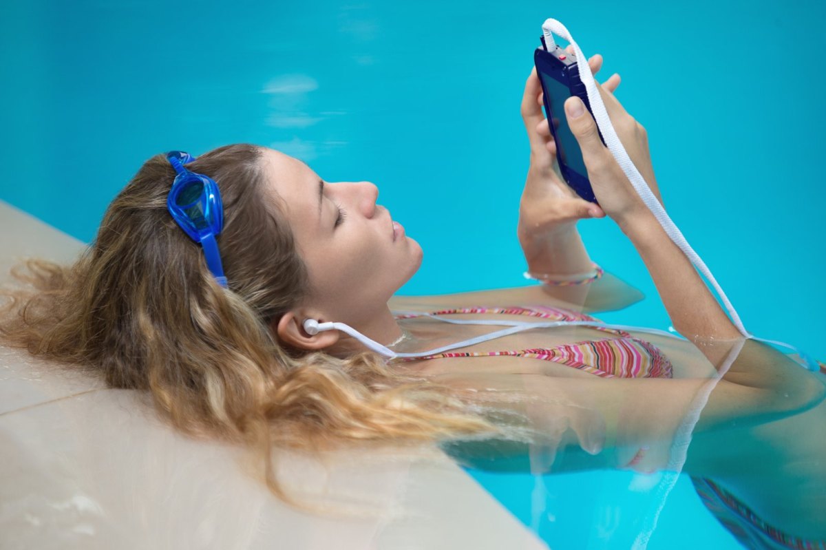 Frau liegt im Pool mit Handy und Kopfhörern.