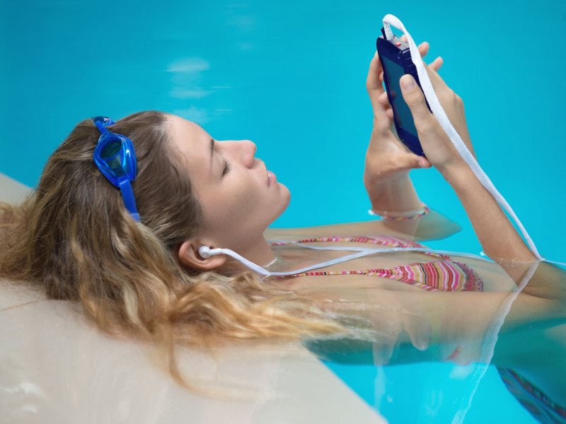 Frau liegt im Pool mit Handy und Kopfhörern.