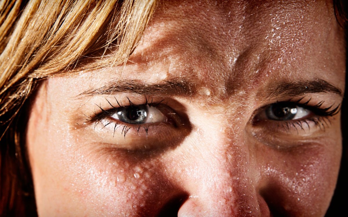 Das Gesicht einer Frau mit Schweißperlen überzogen