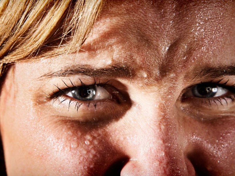 Das Gesicht einer Frau mit Schweißperlen überzogen