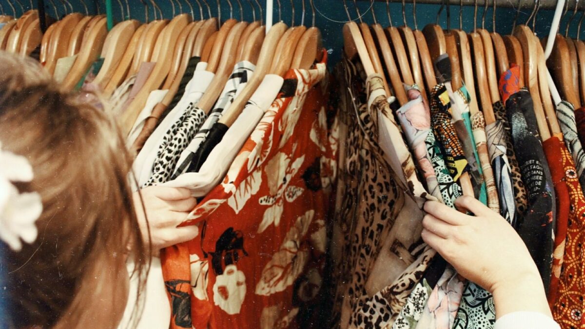 Eine Frau durchsucht einen Kleiderständer mit vielen Kleidungsstücken.