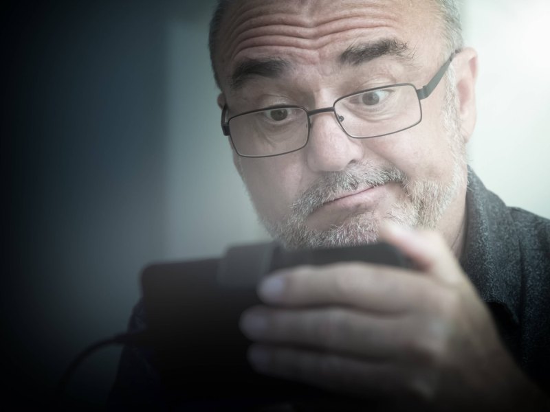 Rentner schaut skeptisch auf ein Smartphone