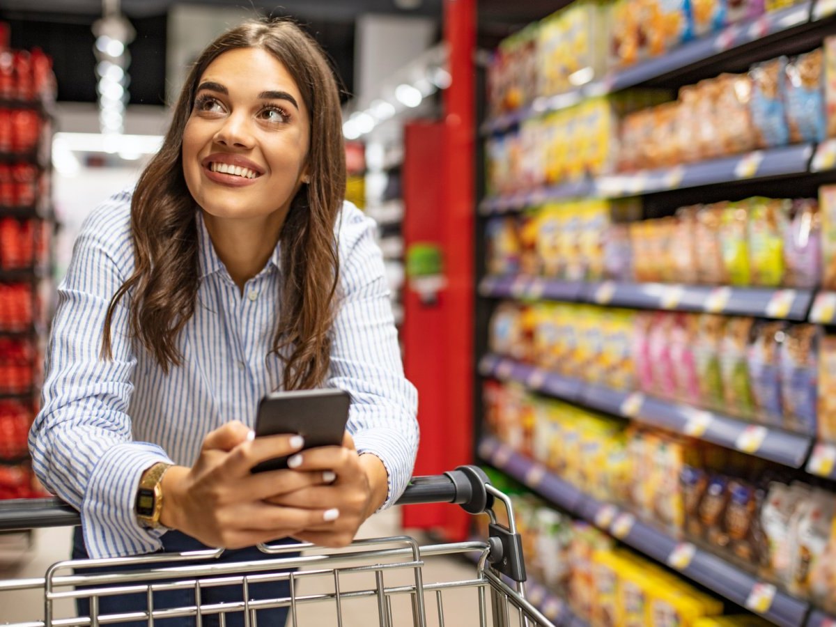 Frau mit Handy am Einkaufswagen
