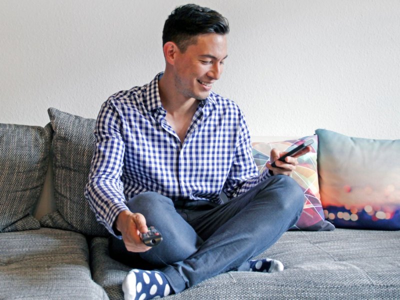 Mann mit Handy und Fernbedienung in der Hand.