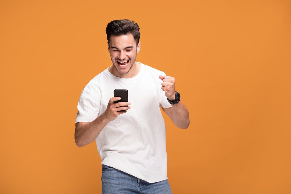 Mann vor orangenem Hintergrund freut sich über seinem Handy.