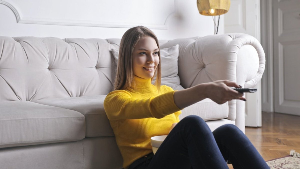 Eine Frau sitzt vor einem Sofa und hat eine Fernbedienung in der Hand.