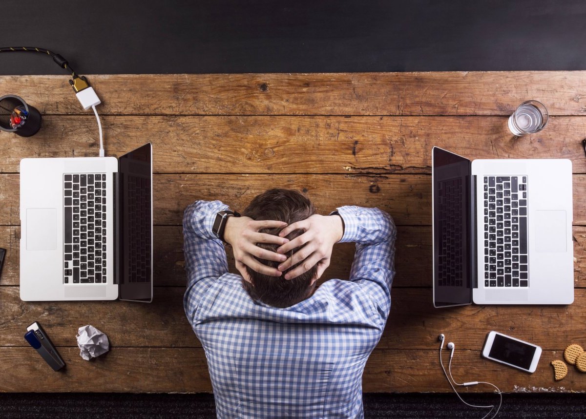 Mann gestresst zwischen zwei Laptops
