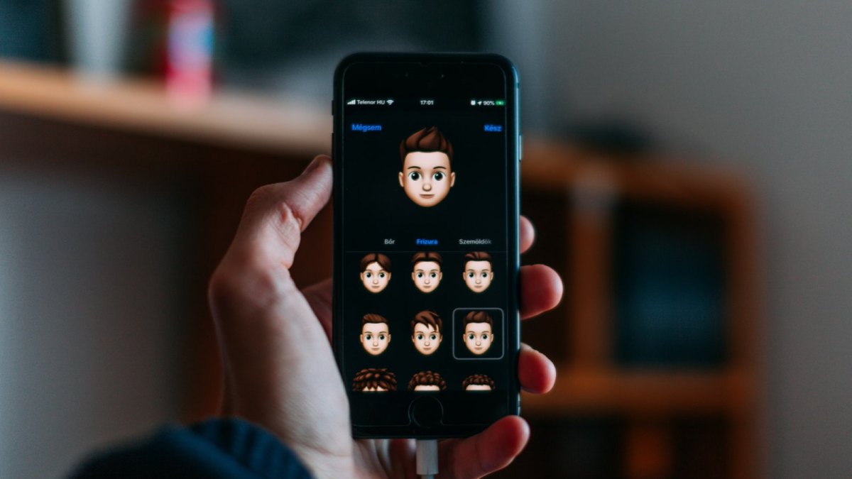 Eine Hand mit einem iPhone auf dem man Memojis sieht.