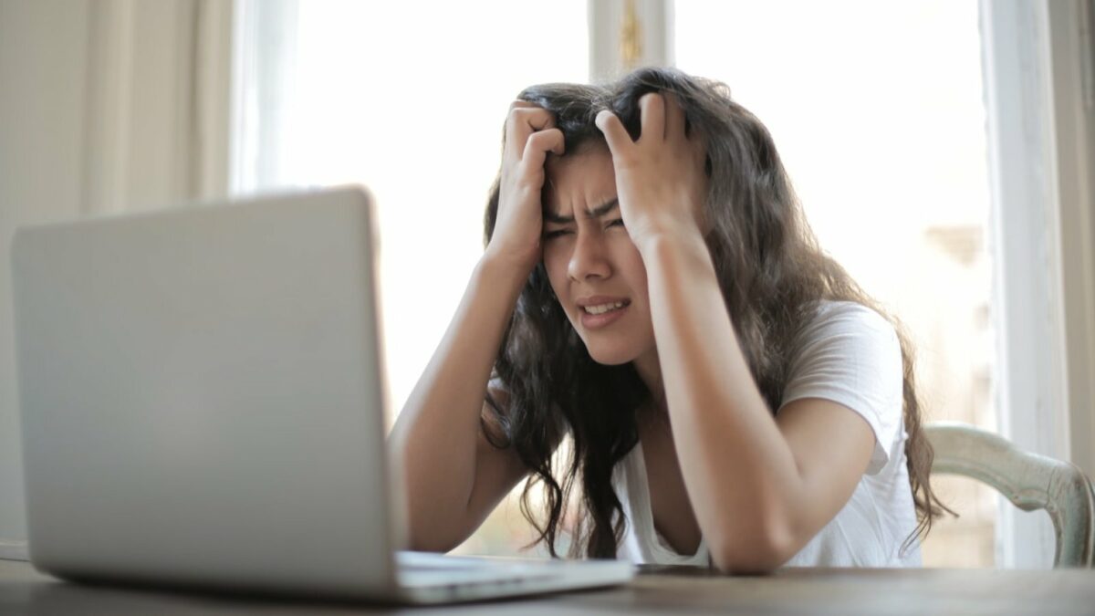 Eine Frau fasst sich vor Verzweiflung an den Kopf und schaut auf ihren Laptop.