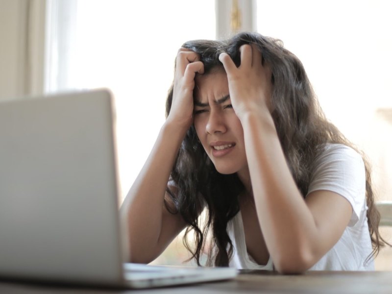 Eine Frau fasst sich vor Verzweiflung an den Kopf und schaut auf ihren Laptop.