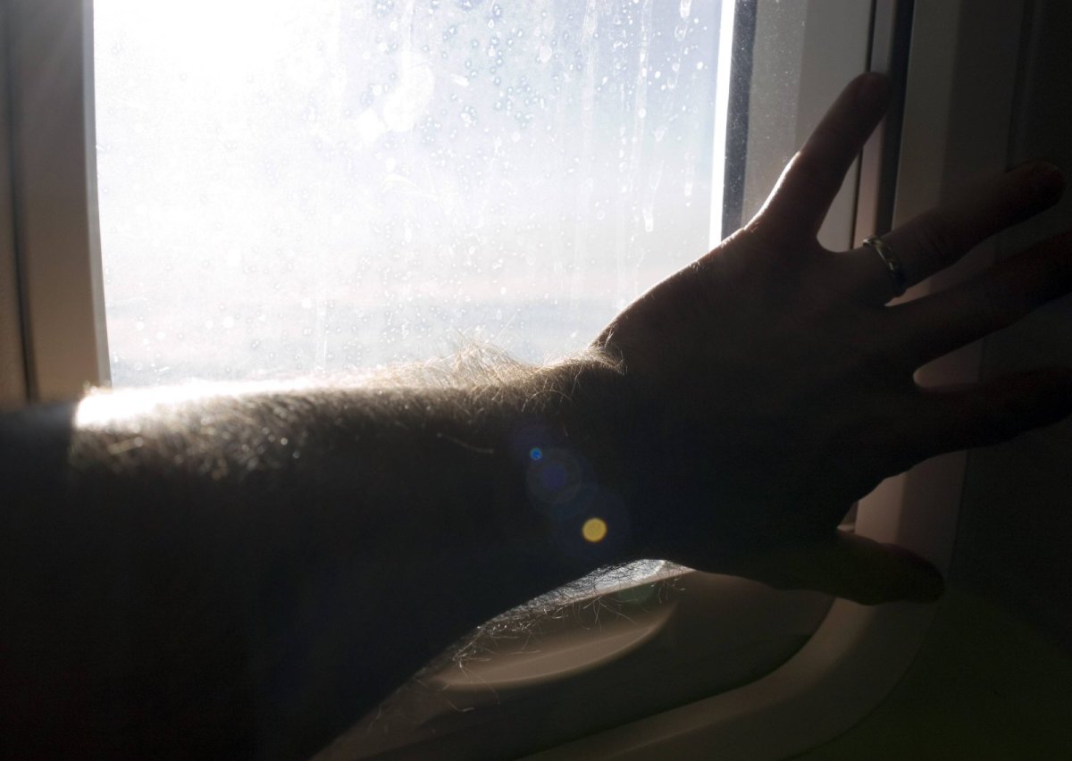 Passagier hält sich bei Turbulenzen am Flugzeugfenster fest.