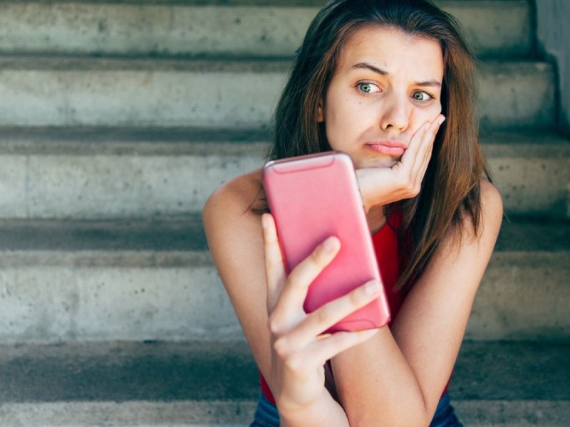 Frau blickt unzufrieden auf ihr Handy.