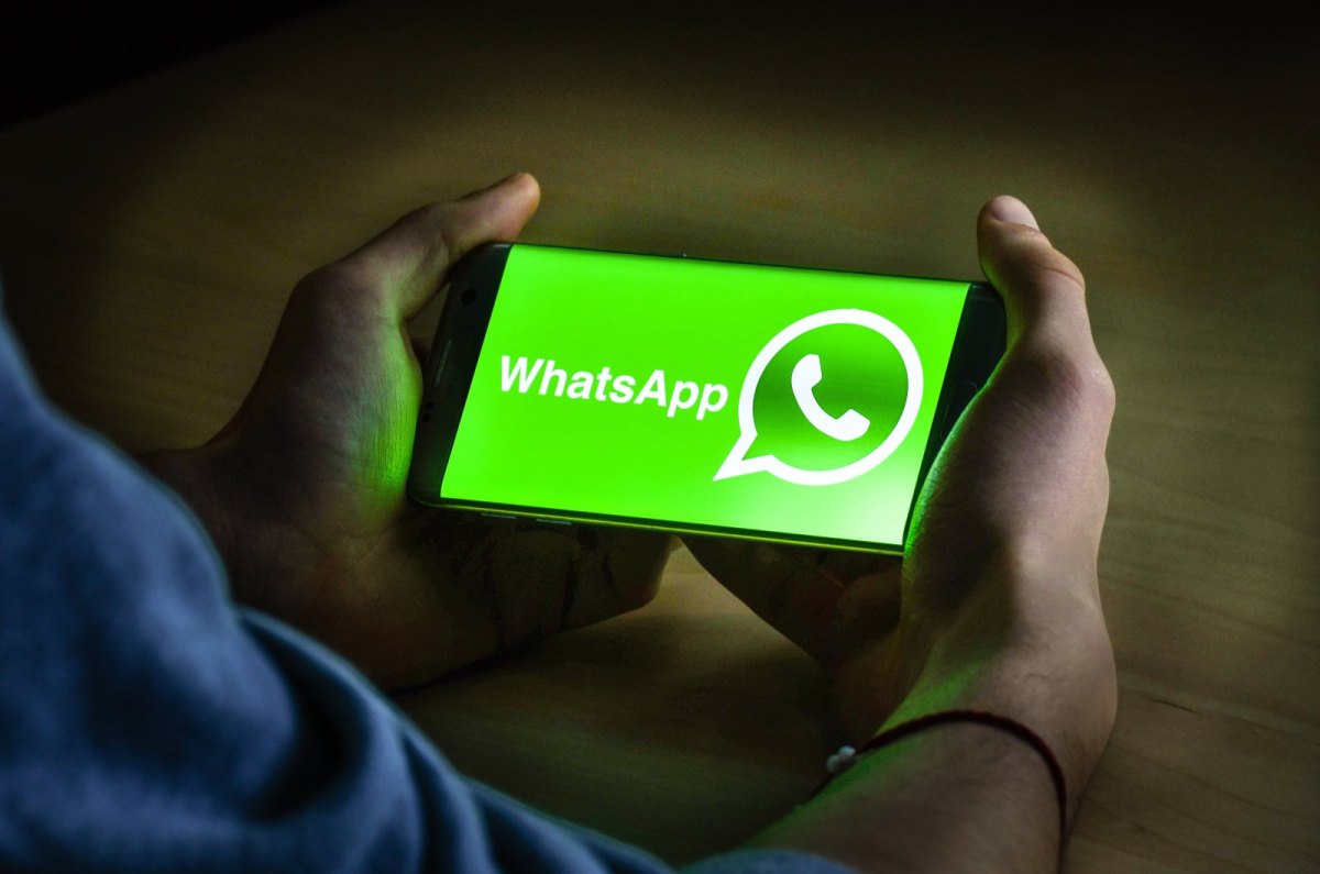 Mann hält Handy mit WhatsApp-Logo auf Display in den Händen.