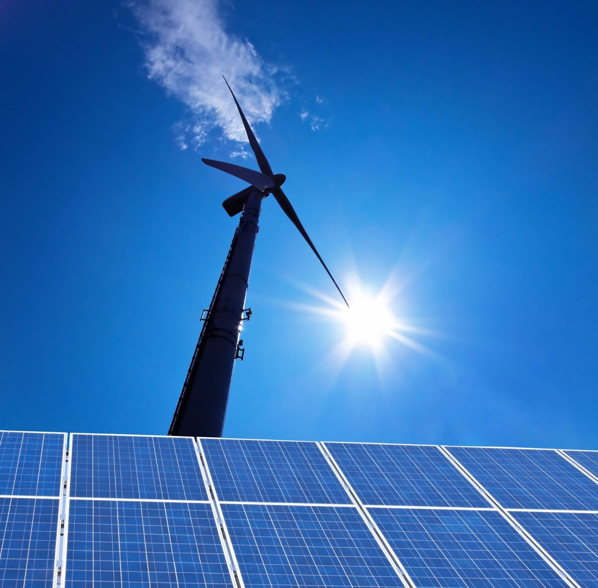 Windrad vor blauem Himmel und Sonne mit Solarpanelen am Boden