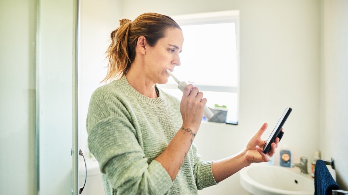 Frau putzt Zähne und hat Handy in der Hand.