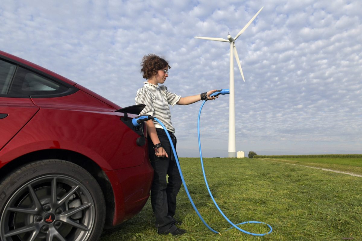 Frau mit Ladekabel von Elektroauto an Windrad