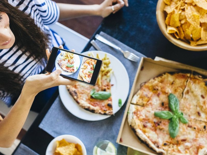 Frau fotografiert ihre Pizza auf dem Tisch.