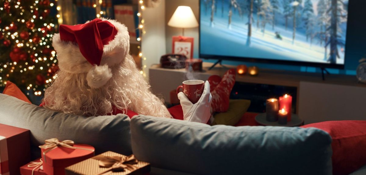 Weihnachtsmann sitzt auf dem Sofa vor dem Fernseher.